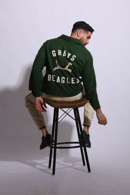 Person wearing a green varsity jacket with 'Beagles' and 'Grays' text, sitting on a chair.