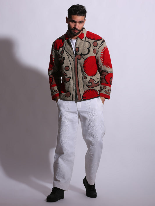 Man wearing a patterned jacket and white pants on a plain background