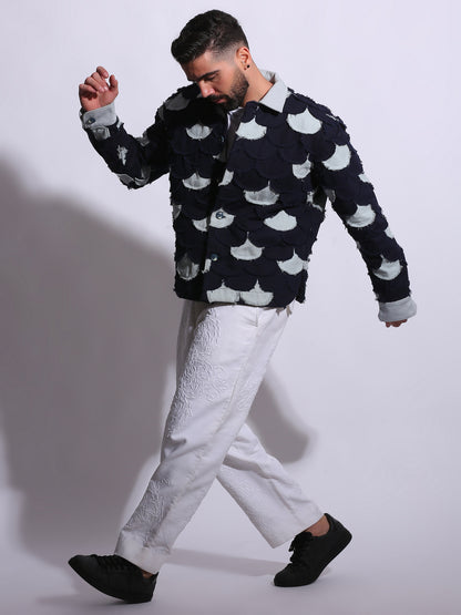 Man wearing a black sweater with white patterns and white pants on a plain background