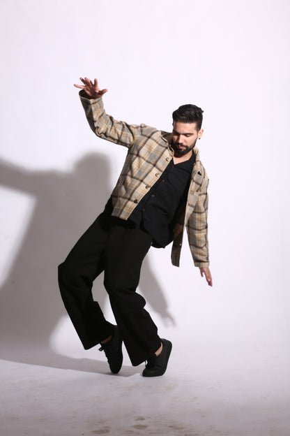 Person in plaid shirt and black pants standing on a white floor with a shadow cast on the wall.