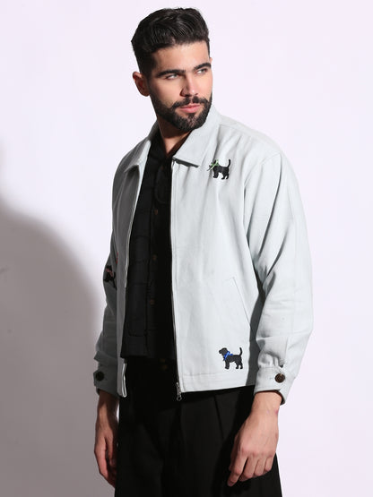 Man wearing a light gray jacket with embroidered dog designs on a plain background