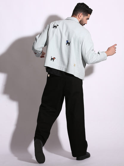 Person wearing a light blue denim jacket with embroidered dog designs on a white background