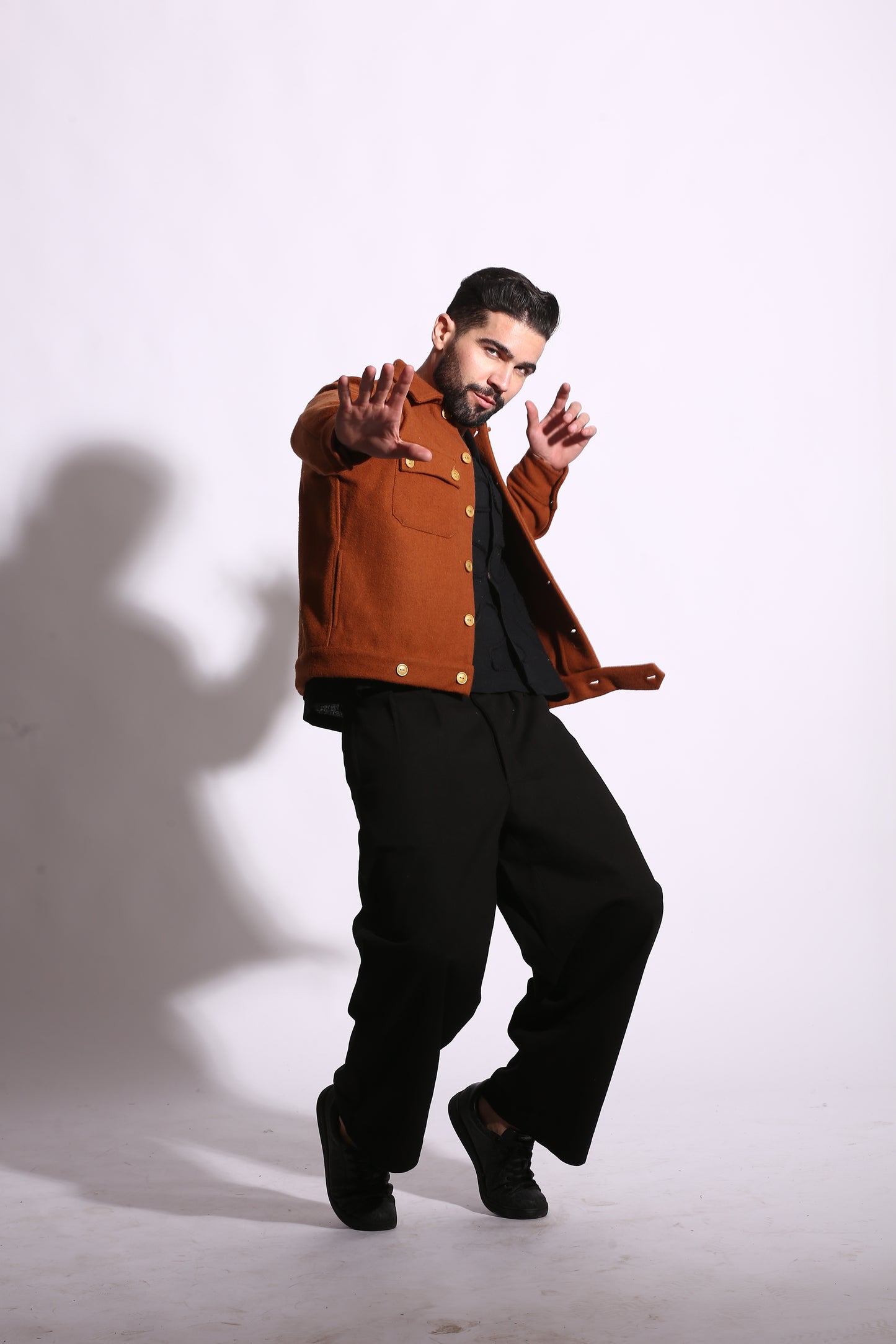 Person wearing a brown jacket and black pants on a white background