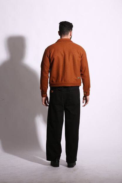 Person wearing a brown jacket and black pants on a white floor.