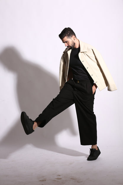 Man in black suit and shoes lying on a white surface with a beige coat.
