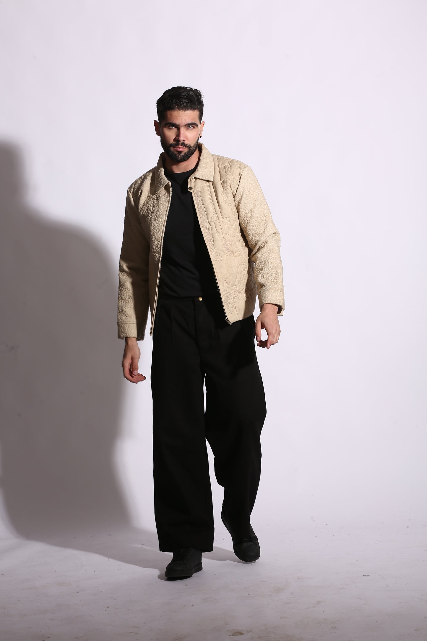 Man wearing a beige jacket and black pants on a white background