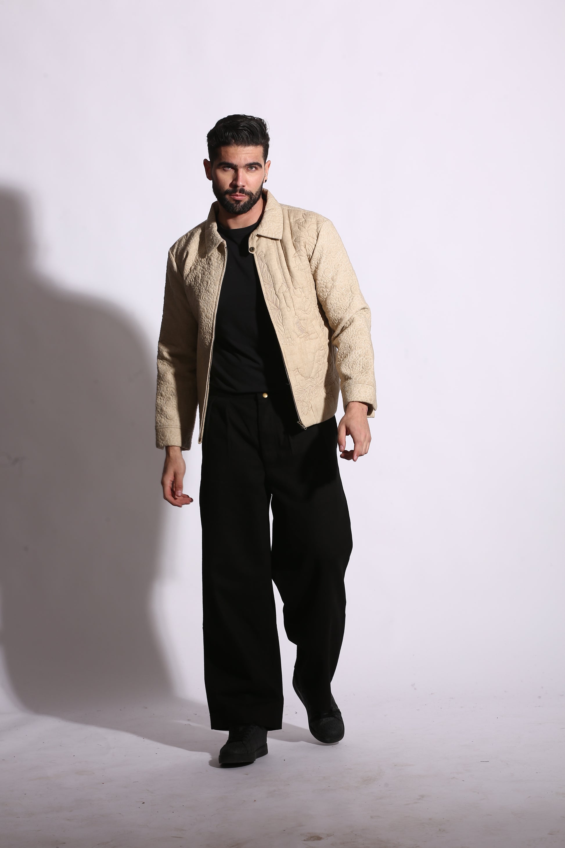 Man wearing a beige jacket and black pants on a white background