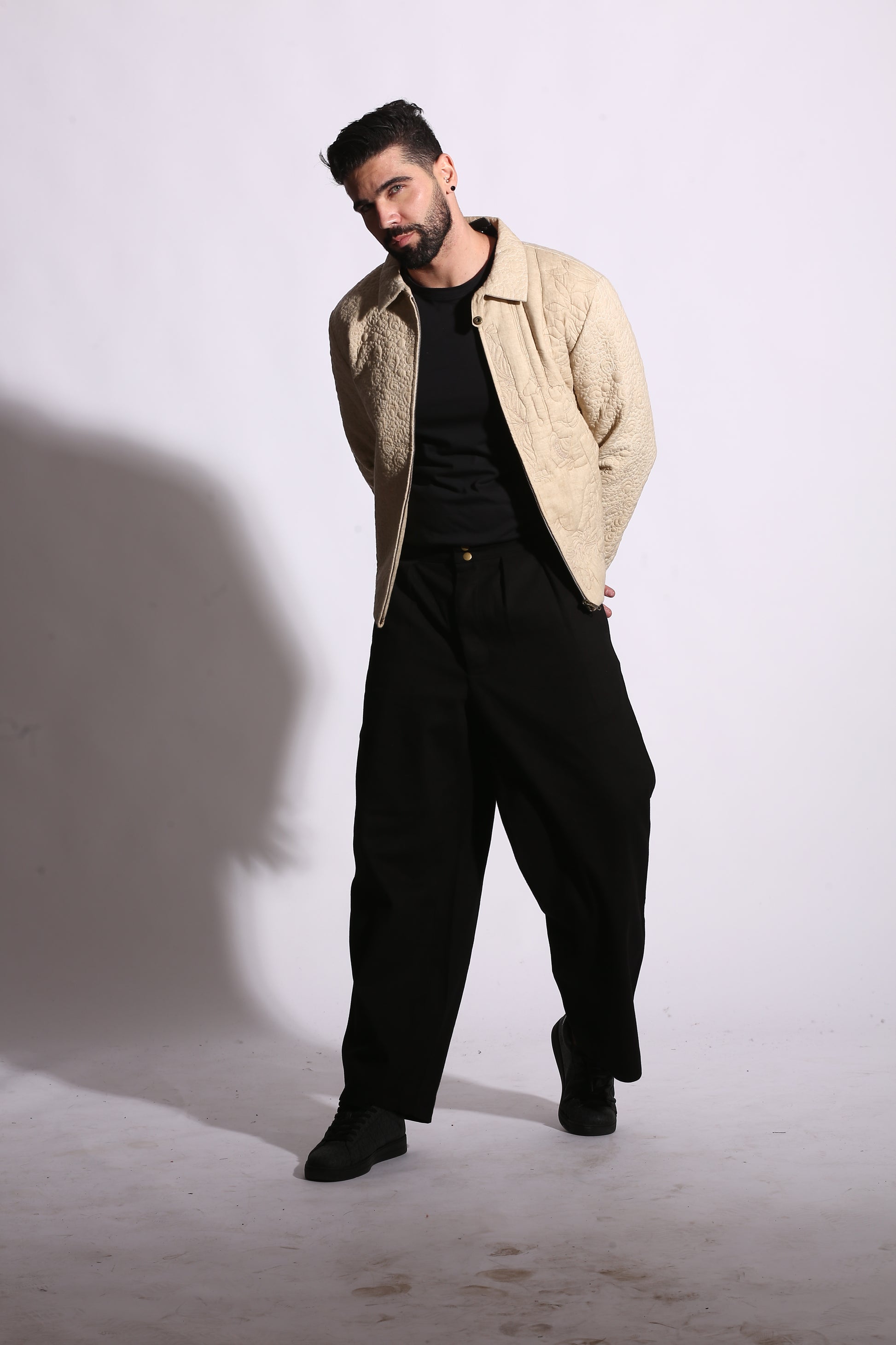 Man wearing a beige jacket and black pants on a white background