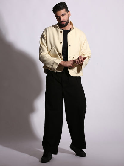 Man wearing a cream jacket over a black shirt and pants on a white background