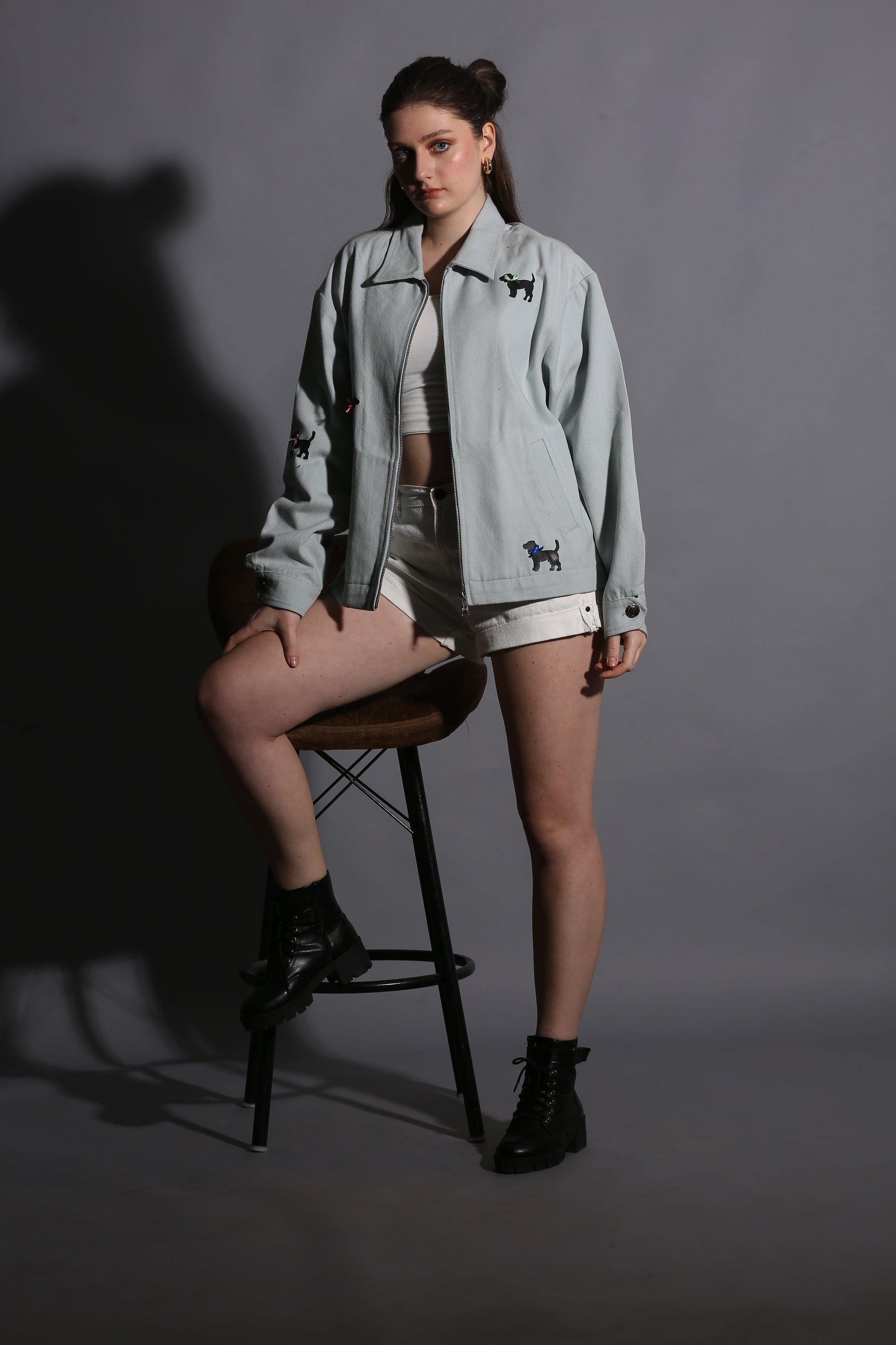 Person wearing a light gray jacket with a dark logo on a gray background