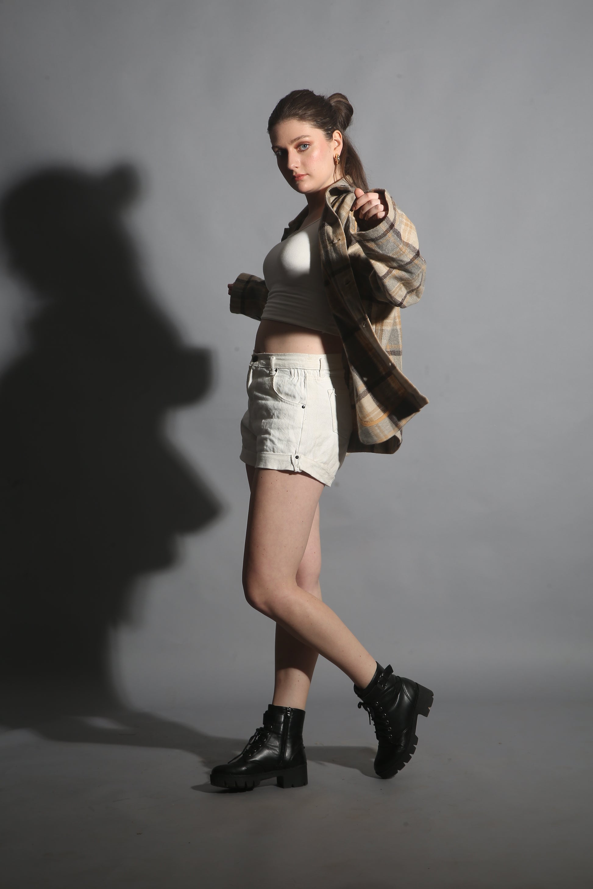 Person wearing a coat and boots with a dramatic shadow on a gray background