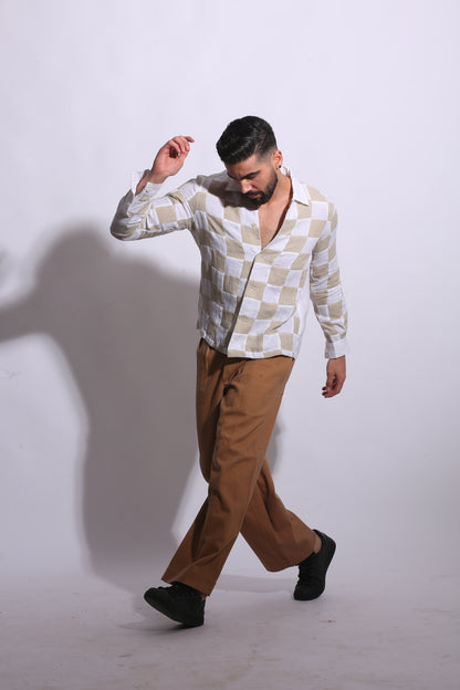 A long-sleeved button-down shirt featuring a large-scale checkerboard patchwork design in neutral sand and off-white linen fabric.