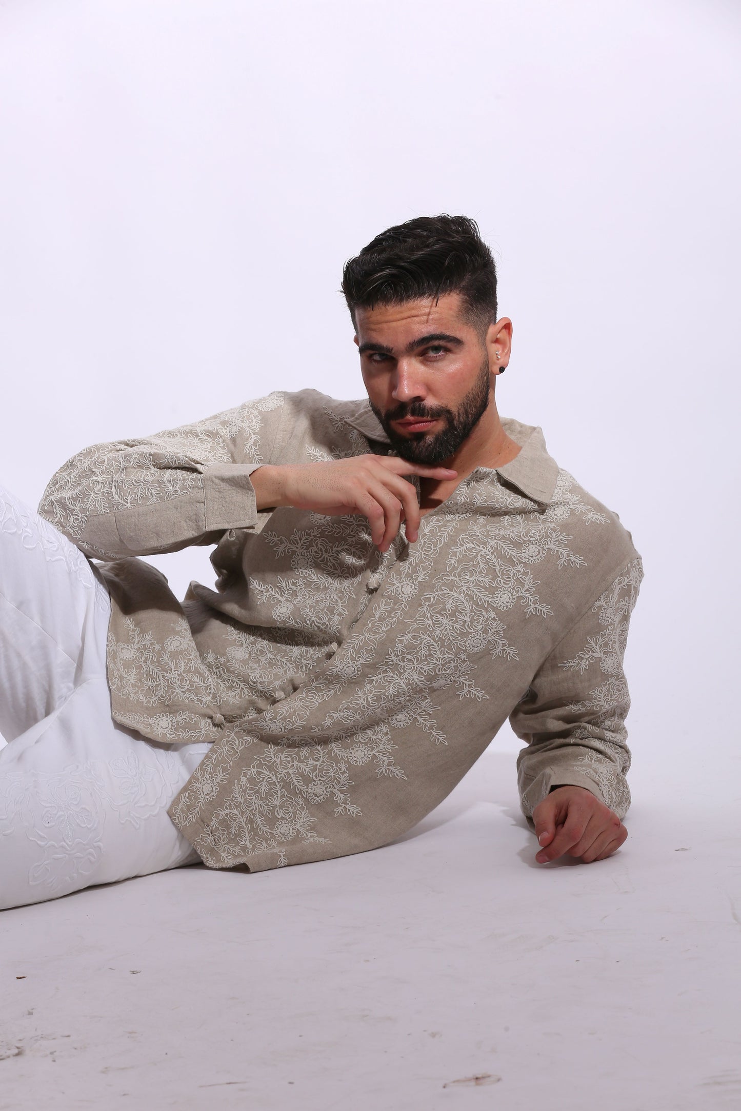Full-length view of a male model posing in an embroidered tan linen shirt with a modern, high-end vacation aesthetic.