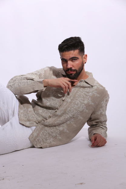 Full-length view of a male model posing in an embroidered tan linen shirt with a modern, high-end vacation aesthetic.