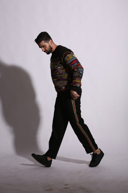Man in a patterned shirt and black pants standing against a white wall with a shadow.