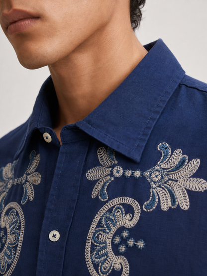 Close-up of a person wearing a navy blue button-up shirt with ornate white and light blue embroidery on the chest and collar.